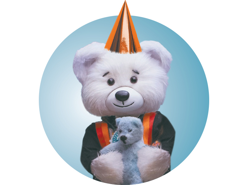 Photo of Spirit Bear wearing an orange foil party hat and holding his Jordan's Principle teddy bear