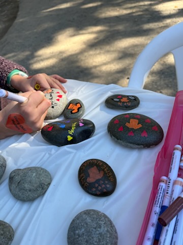 Child drawing hearts and an orange shirt on a rock for Orange Shirt Day