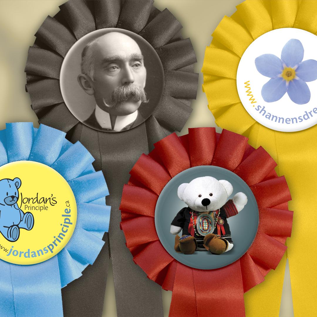 photo of a collection of colourful prize ribbons. Each ribbon has a circular image in the middle of the ruffle that represents the paricular award – the Jordan’s Principle logo, a photo of Peter Henderson Bryce, a photo of Spirit Bear, a photo of a forget-me-not (for Shannen’s Dream).